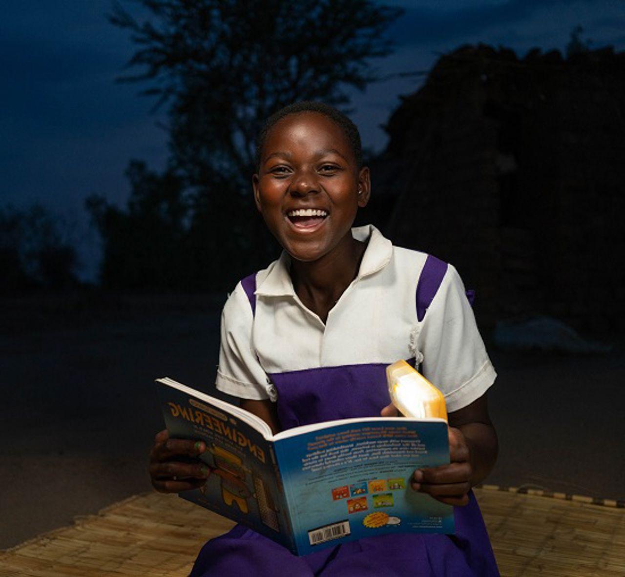 Girl looking into the camera smiling, holding a book